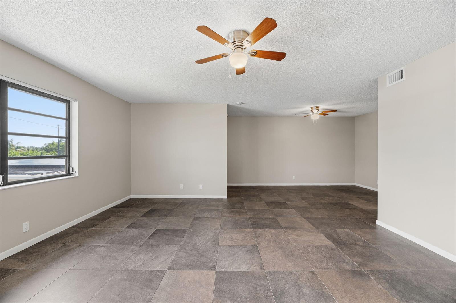 An empty room features large dark floor tiles, beige walls, and two ceiling fans — 1769 NE 40th Place # 506, Pompano Beach FL 33064, POMPANO BEACH, FL