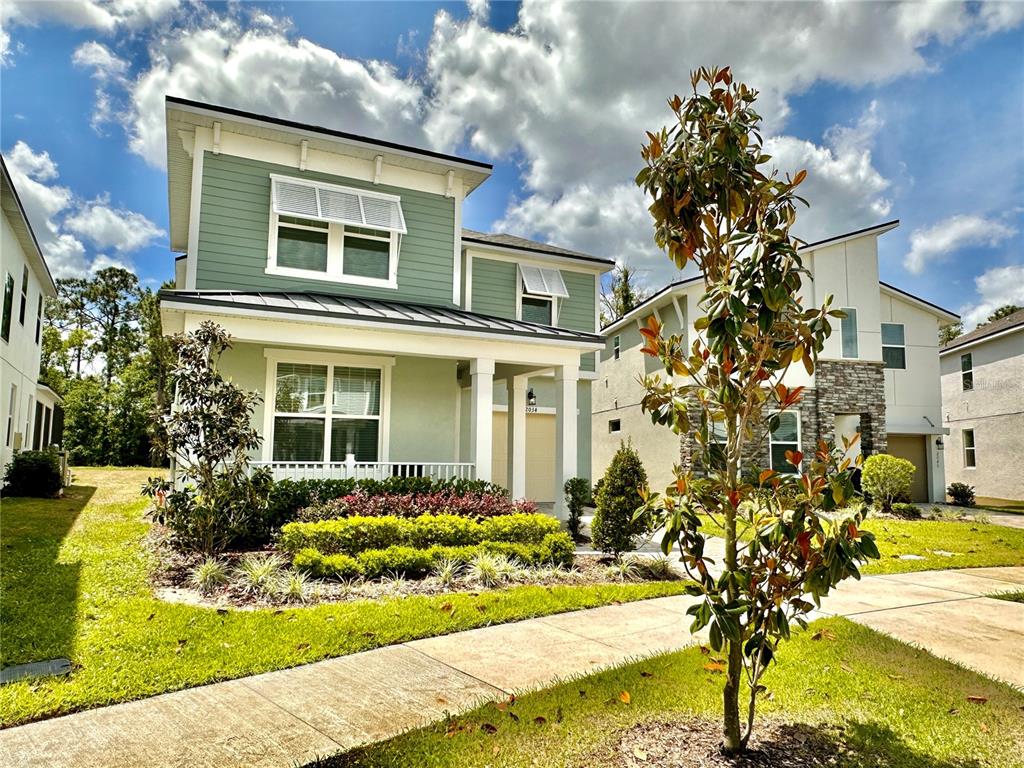 A two-story green house with a front porch and a small tree in the yard — 2034 FLEMING MIST PLACE, KISSIMMEE, FL