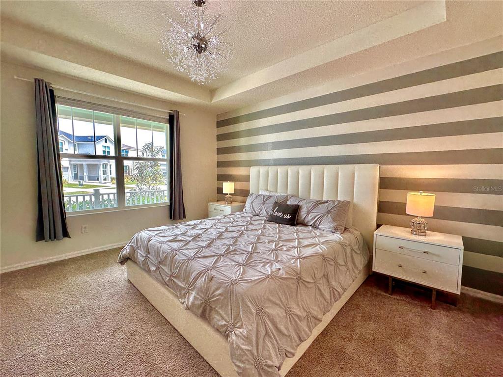 A bedroom features a tufted headboard, striped accent wall, and a crystal chandelier — 2034 FLEMING MIST PLACE, KISSIMMEE, FL