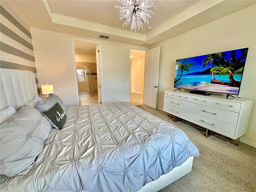 A bedroom features a tufted headboard, a large television on a white dresser, and a chandelier — 2034 FLEMING MIST PLACE, KISSIMMEE, FL