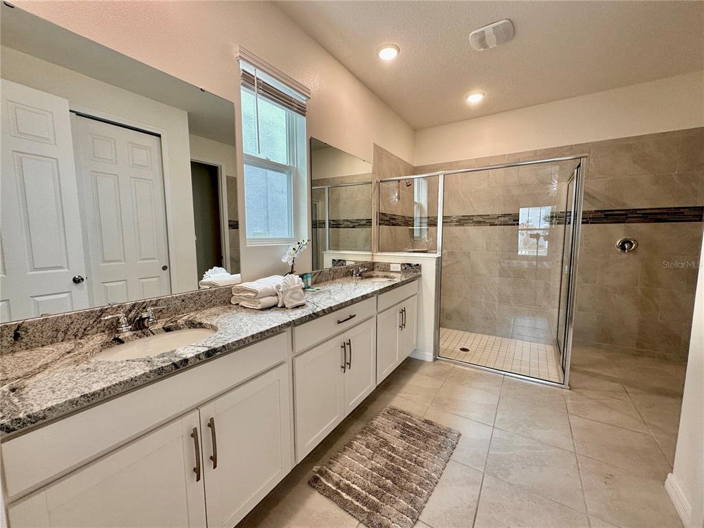 A bathroom features a double vanity with granite countertops, white cabinets, and a tiled walk-in shower — 2034 FLEMING MIST PLACE, KISSIMMEE, FL