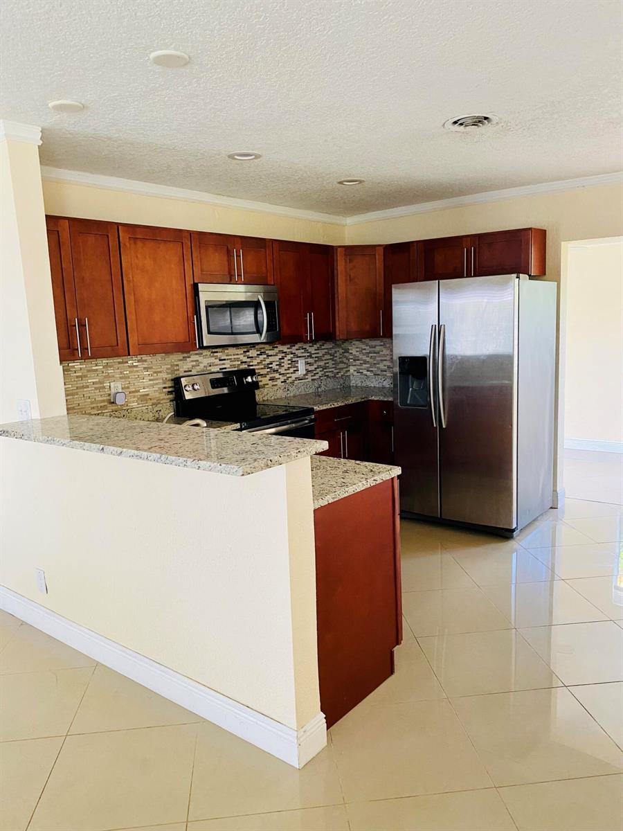 A kitchen features wood cabinets, granite countertops, stainless steel appliances, and light-colored tile flooring — 4559 NW 16th Way, Tamarac FL 33309, TAMARAC, FL