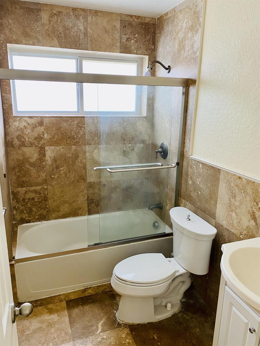 A bathroom features a bathtub with a glass sliding door, tiled walls, and a toilet — 4559 NW 16th Way, Tamarac FL 33309, TAMARAC, FL