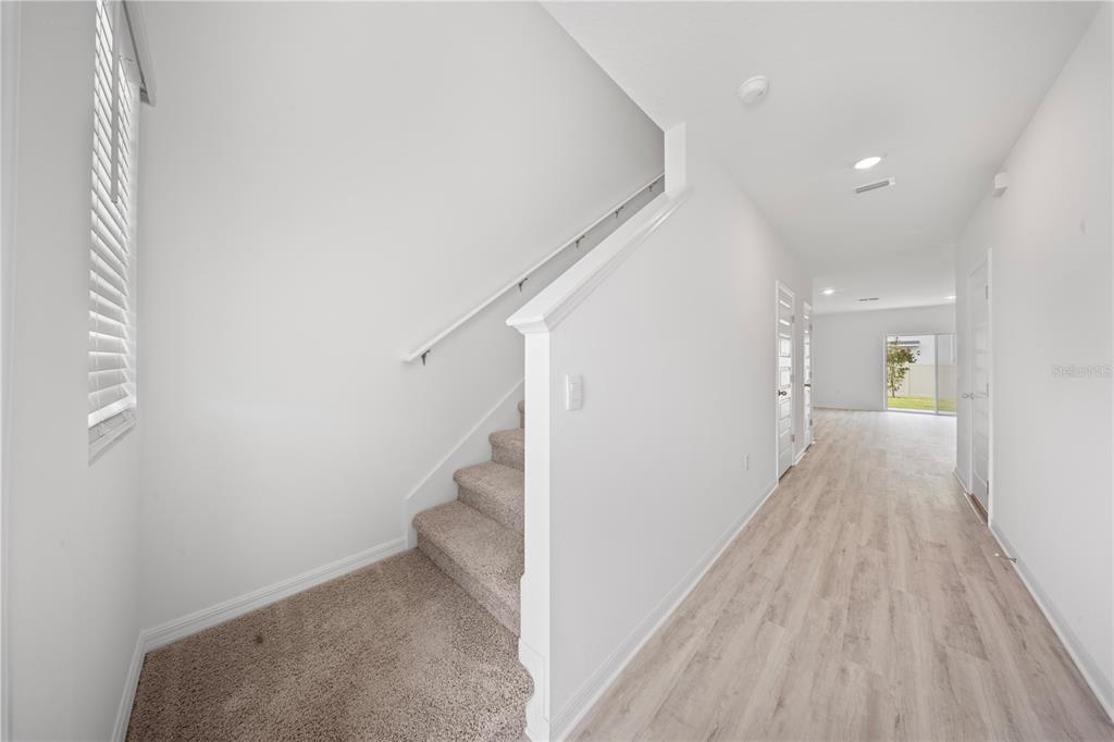 An entryway features a carpeted staircase, light wood-look flooring, and white walls — 4348 BUTTERSCOTCH CIRCLE, LAKELAND, FL