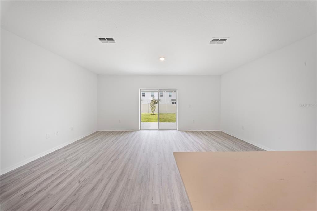 An empty living room with light wood-look flooring, white walls, and sliding glass patio doors — 4348 BUTTERSCOTCH CIRCLE, LAKELAND, FL