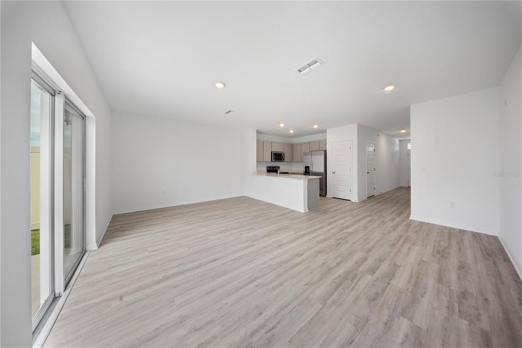 An open-concept living area features light wood-look flooring, white walls, and a kitchen with stainless appliances — 4348 BUTTERSCOTCH CIRCLE, LAKELAND, FL