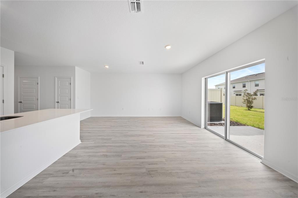 An open-concept living area features light wood-look flooring, white walls, and sliding glass patio doors — 4348 BUTTERSCOTCH CIRCLE, LAKELAND, FL