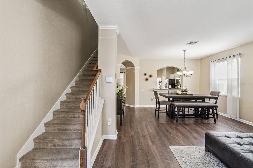 A staircase with carpeted steps leads up next to a dining area with wood flooring — 7759 TOSTETH STREET, KISSIMMEE, FL