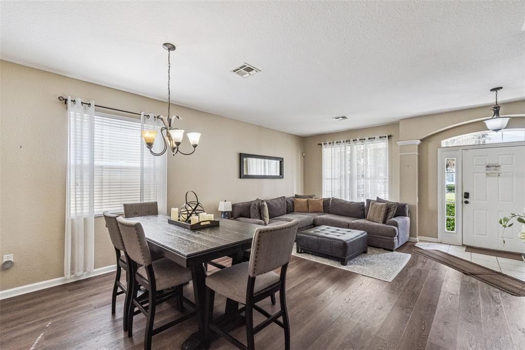 An open-concept dining and living area features wood-look flooring, a sectional sofa, and a chandelier — 7759 TOSTETH STREET, KISSIMMEE, FL
