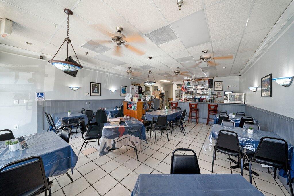 A restaurant interior with blue-covered tables, black chairs, ceiling fans, and a bar area — 3092 S Jog Road, FL 33463, FL