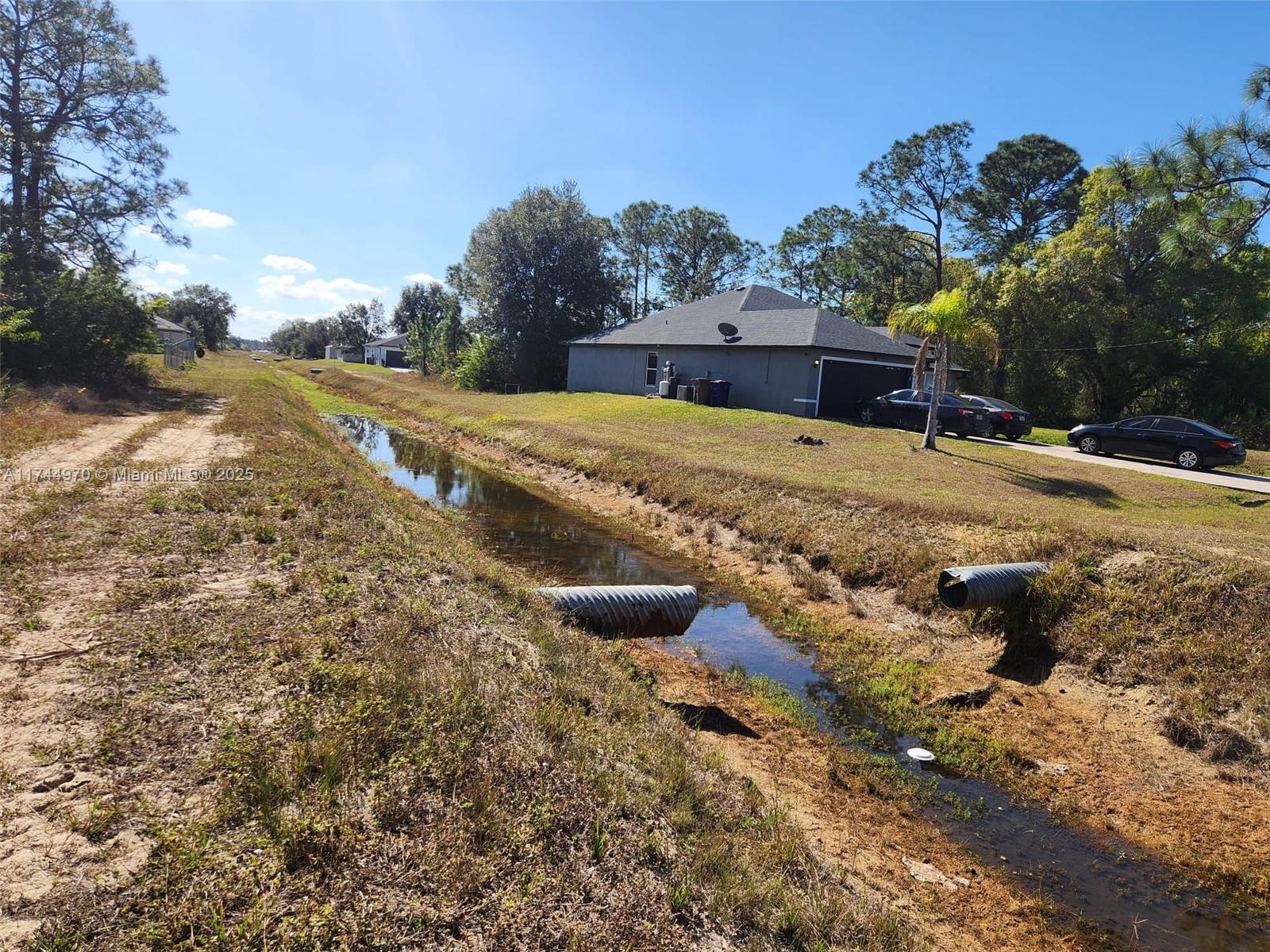 A drainage ditch runs alongside a residential house with a driveway and parked cars — 2719 50 W, Lehigh Acres FL 33971, LEHIGH ACRES, FL
