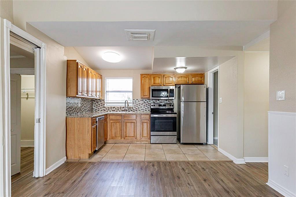 A kitchen features wood cabinets, stainless steel appliances, granite countertops, and a tiled floor — 7216 E EMMA STREET, TAMPA, FL