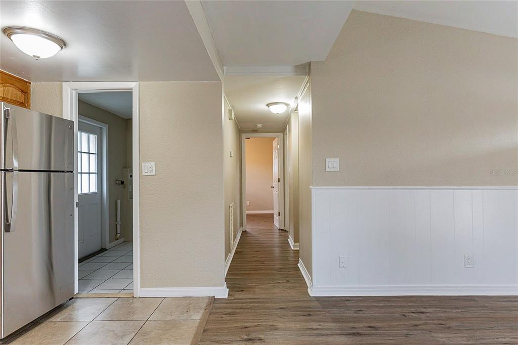 A hallway with wood-look flooring leads to a room, adjacent to a kitchen with tile — 7216 E EMMA STREET, TAMPA, FL