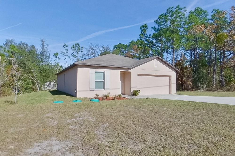 A single-story, light-colored stucco house with a two-car garage sits on a grassy lot — 2799 W SHEILA DRIVE, CITRUS SPRINGS, FL