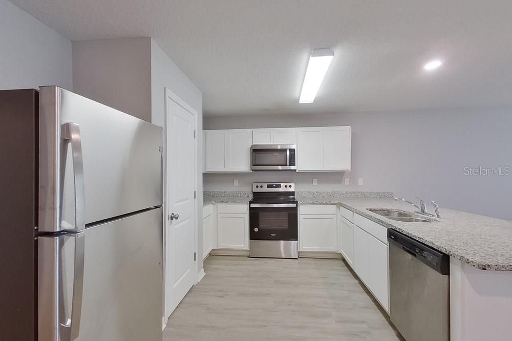 A kitchen features white cabinets, granite countertops, stainless steel appliances, and light wood-look flooring — 2799 W SHEILA DRIVE, CITRUS SPRINGS, FL