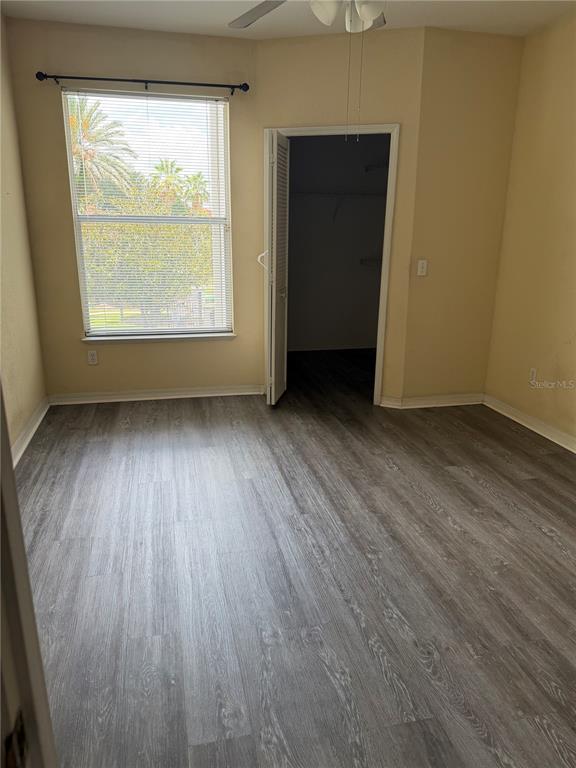An empty bedroom features light-colored walls, gray wood-look flooring, a window, and a walk-in closet — 2740 MAITLAND CROSSING WAY UNIT 207, ORLANDO, FL