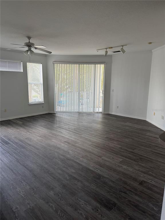 An empty living room features dark wood-look flooring, a ceiling fan, and sliding glass doors — 2740 MAITLAND CROSSING WAY UNIT 207, ORLANDO, FL