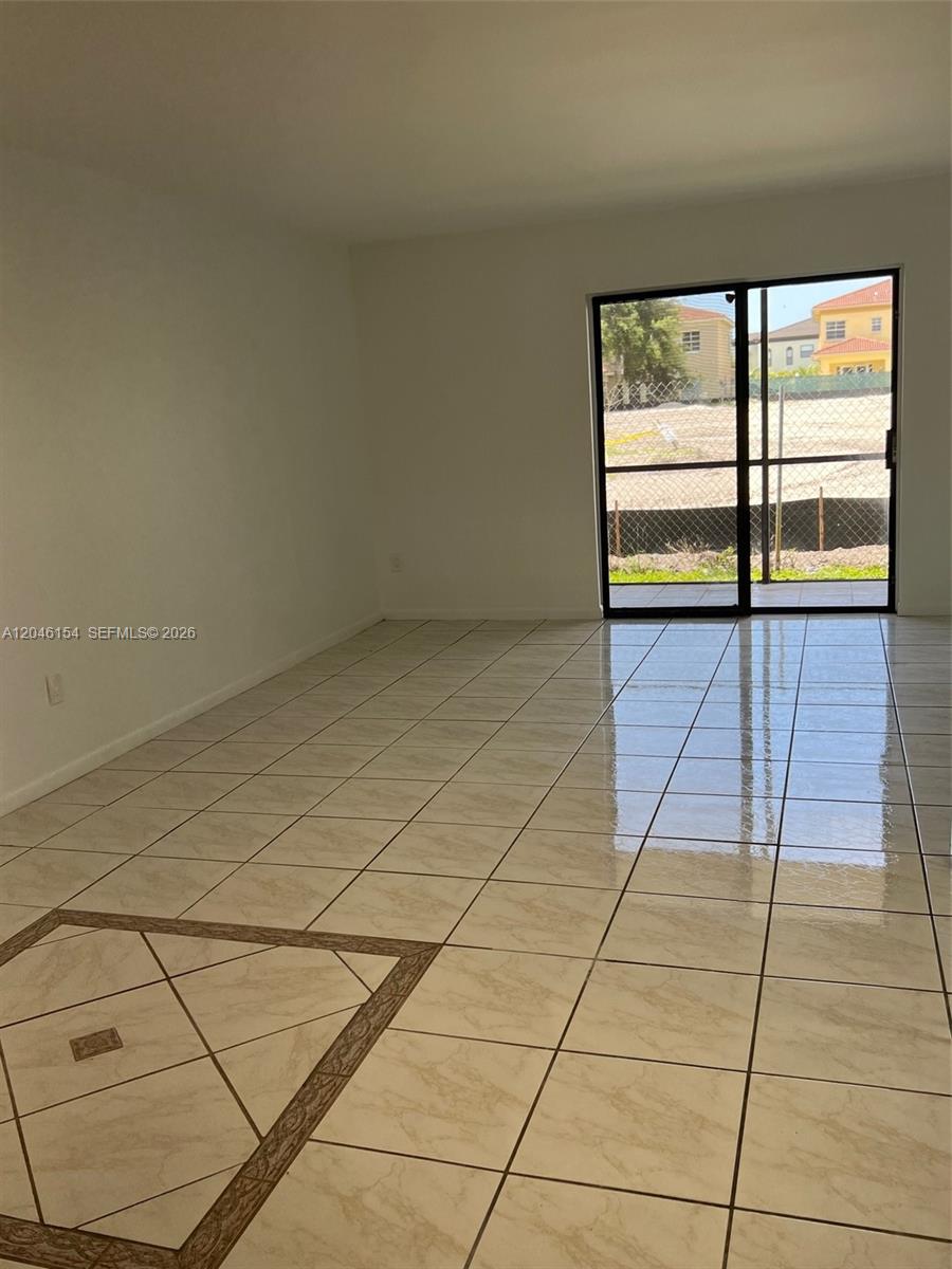 An empty room features light-colored tile flooring with a decorative border and a sliding glass door — 852 NE 209th St # 38, Miami FL 33179, MIAMI, FL