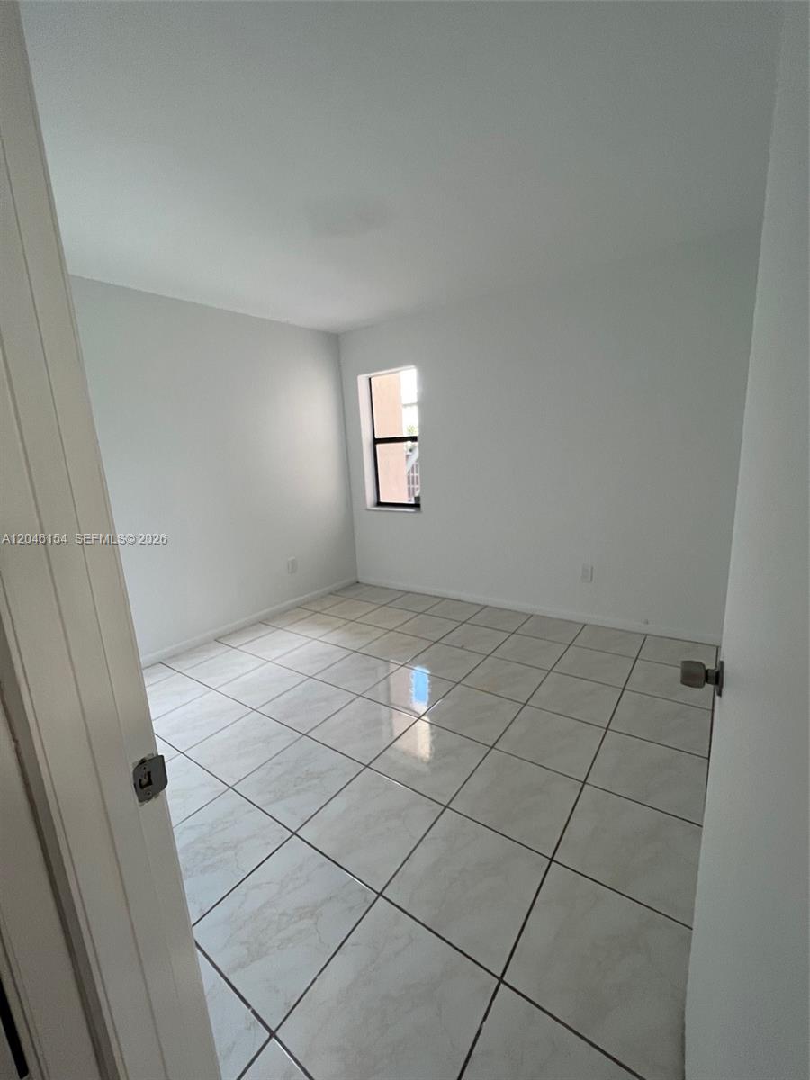 An empty bedroom features white walls, a single window, and light-colored tiled flooring — 852 NE 209th St # 38, Miami FL 33179, MIAMI, FL