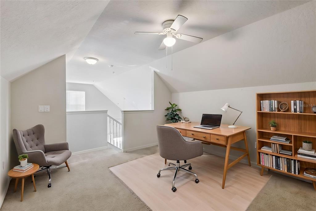 A carpeted home office features a wooden desk, a gray chair, and a bookshelf — 5959 WESTGATE DRIVE UNIT 1527, ORLANDO, FL