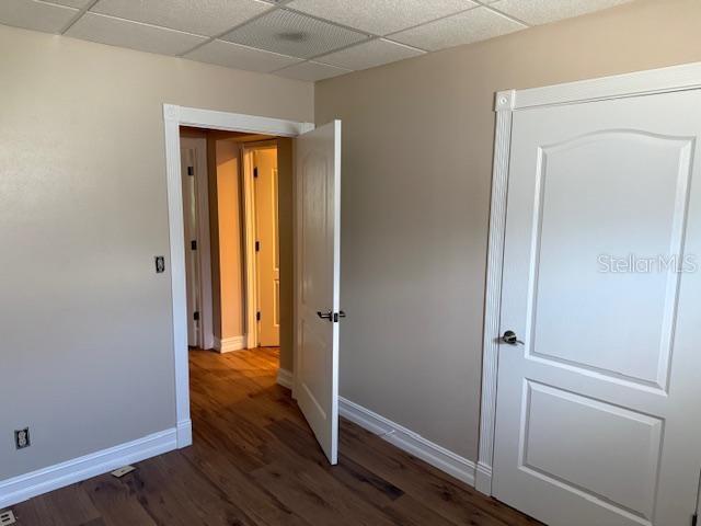 An interior room with light walls, wood-look flooring, a ceiling grid, and two white doors — 228 NEW YORK AVENUE E UNIT C, DELAND, FL