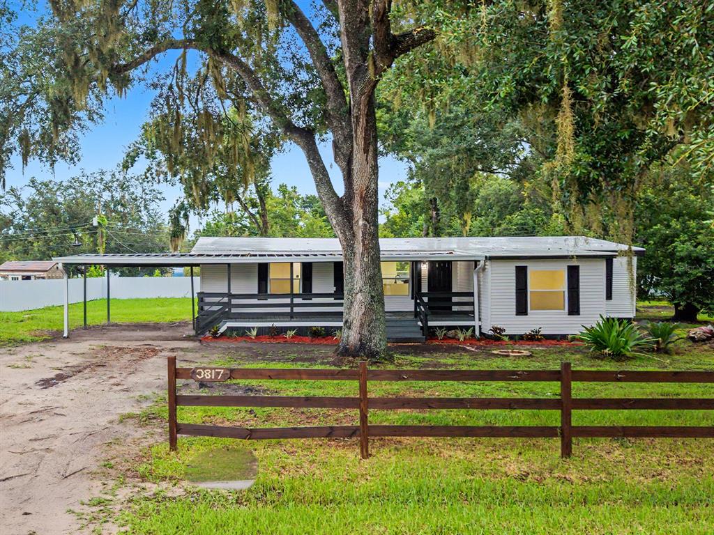 A single-story house with a carport and a wooden fence sits under a large tree — 3817 WARD ROAD, LAKELAND, FL