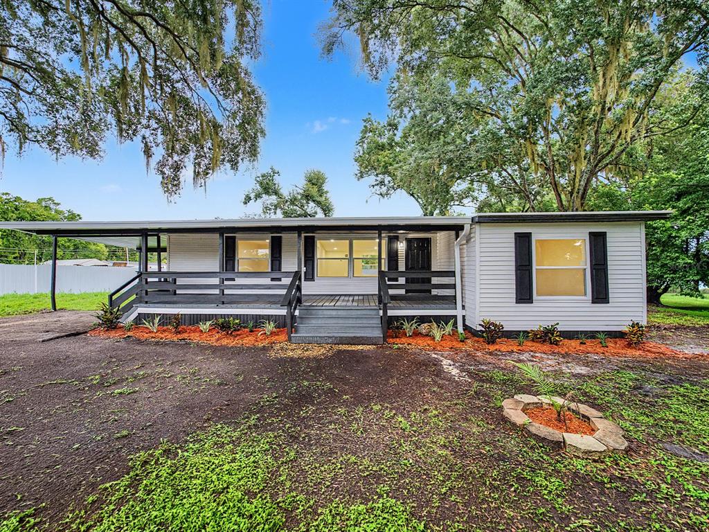 A single-story house with white siding, a dark wooden deck, and a covered carport — 3817 WARD ROAD, LAKELAND, FL