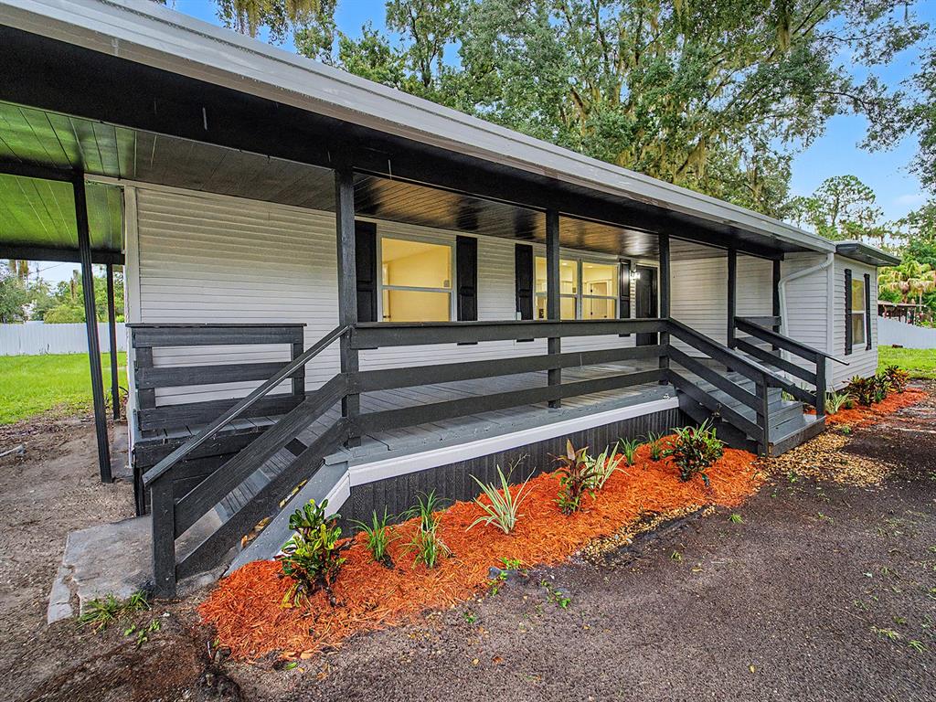 A white house with a dark-painted porch, wooden railings, and a landscaped mulch bed — 3817 WARD ROAD, LAKELAND, FL