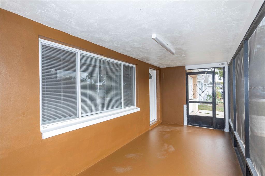 A covered patio with brown painted walls and floor, a large window, and a screen door — 6149 2ND AVENUE, NEW PORT RICHEY, FL