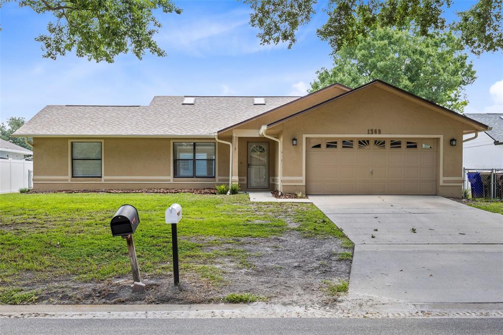 A single-story tan house with a two-car garage and a front lawn with two mailboxes — 1369 WOOD LAKE CIRCLE, ST CLOUD, FL