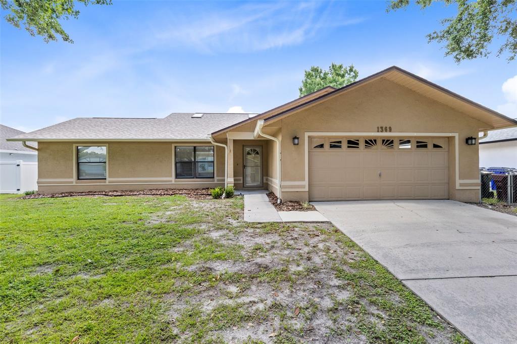 A single-story tan house with a two-car garage and a concrete driveway — 1369 WOOD LAKE CIRCLE, ST CLOUD, FL
