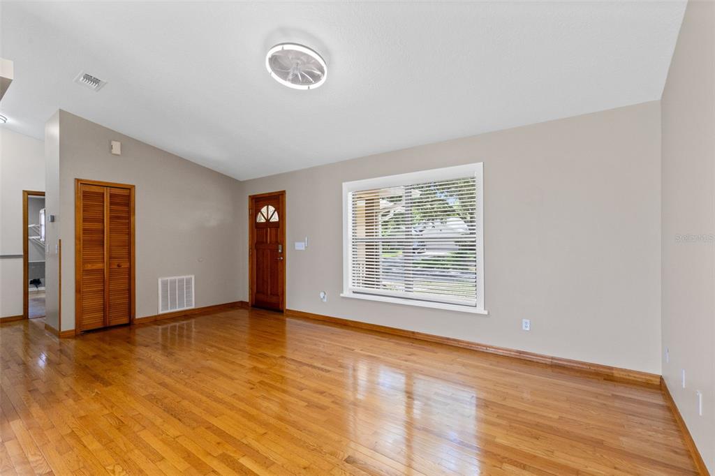 An empty living room features hardwood floors, a large window, and a wooden front door — 1369 WOOD LAKE CIRCLE, ST CLOUD, FL