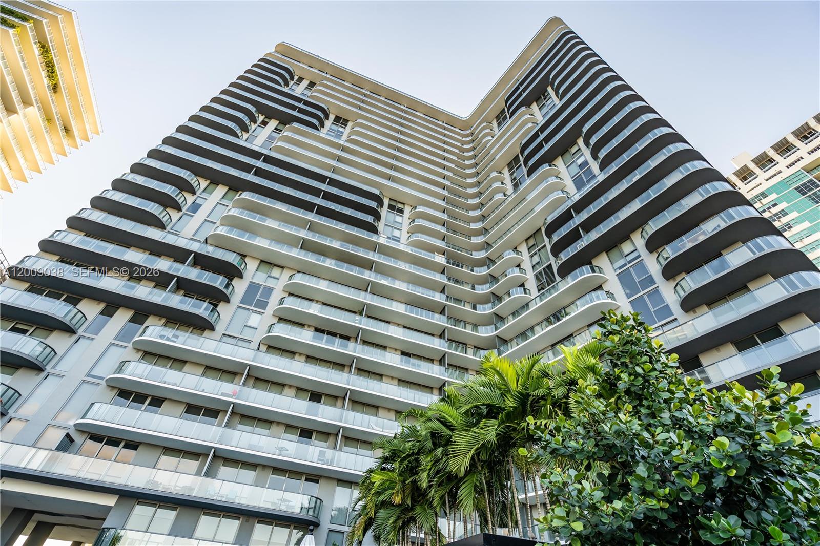 A low-angle view of a modern high-rise residential building with curved glass balconies — 121 NE 34th St # 2810, Miami FL 33137, MIAMI, FL