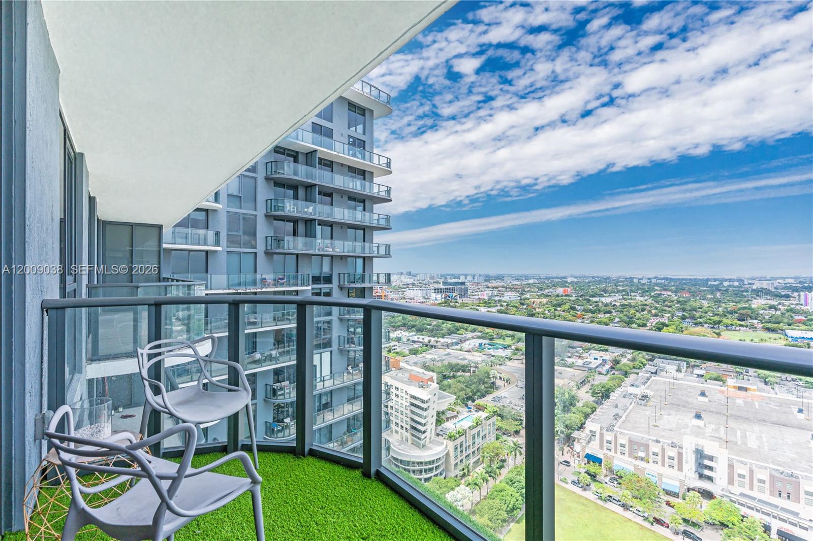A balcony with artificial turf, two chairs, and a glass railing overlooks a city skyline — 121 NE 34th St # 2810, Miami FL 33137, MIAMI, FL