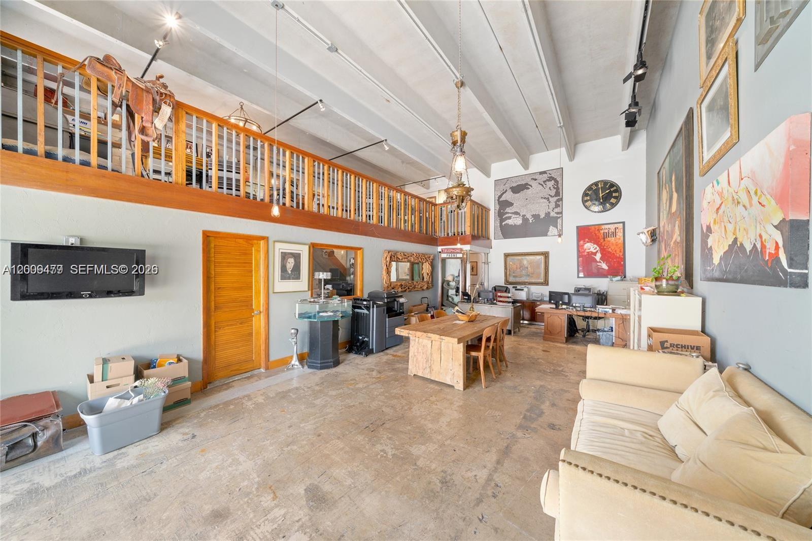 A high-ceilinged room features a wooden loft, concrete floors, office furniture, and eclectic wall art — 5582 NE 4th Ct # 6A, Miami FL 33137, MIAMI, FL