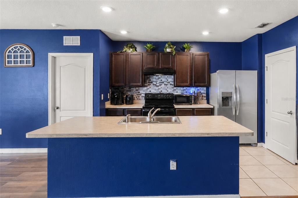 A kitchen features a blue island, dark wood cabinets, stainless steel appliances, and blue walls — 931 SUMMER GLEN DRIVE, WINTER HAVEN, FL