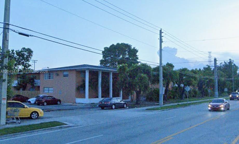 A two-story apartment building with a parking lot sits beside a road with passing cars — 9760 SW 184th St # 12D, Cutler Bay FL 33157, CUTLER BAY, FL