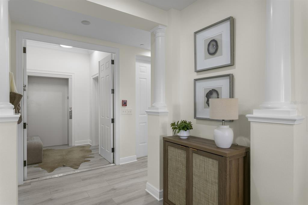 A hallway features light wood flooring, white columns, a wooden cabinet, and framed wall art — 43 BAYVIEW COURT S UNIT A, ST PETERSBURG, FL