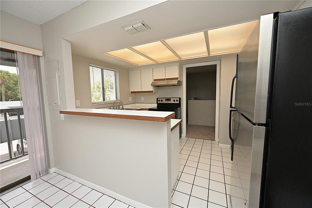 A kitchen features white cabinets, a breakfast bar, tile flooring, and a stainless steel refrigerator — 1808 VILLAGE COURT, MULBERRY, FL