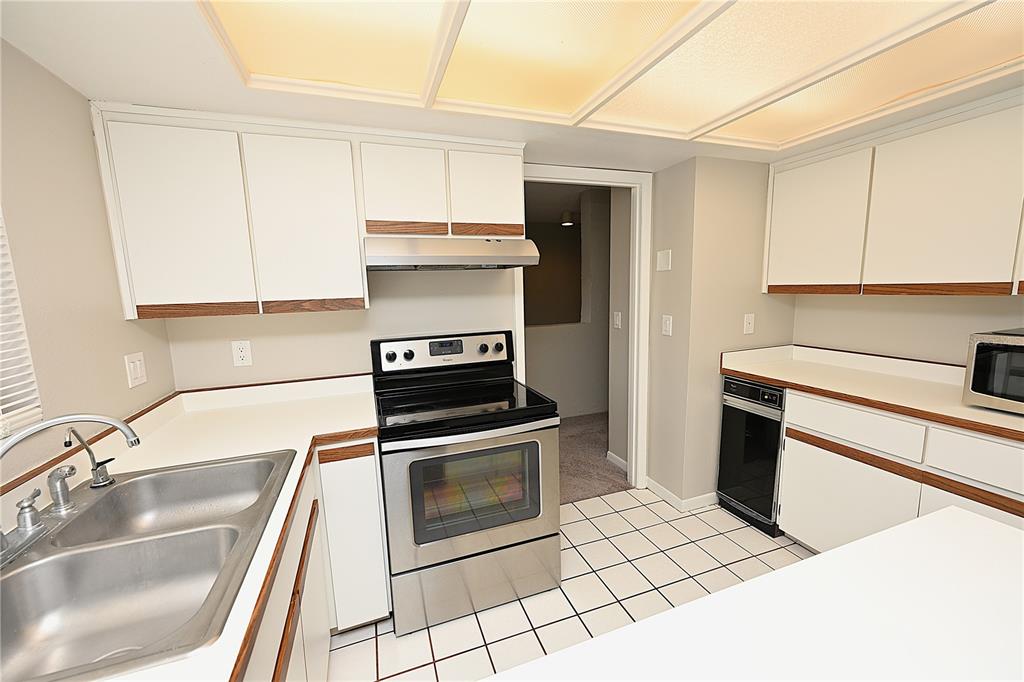 A kitchen features white cabinets with wood trim, stainless steel appliances, and white tiled flooring — 1808 VILLAGE COURT, MULBERRY, FL