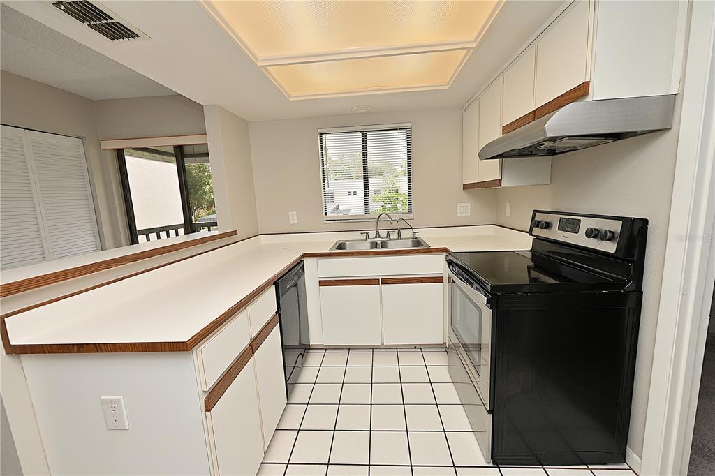 A kitchen with white cabinets, wood trim, white countertops, black appliances, and tiled flooring — 1808 VILLAGE COURT, MULBERRY, FL
