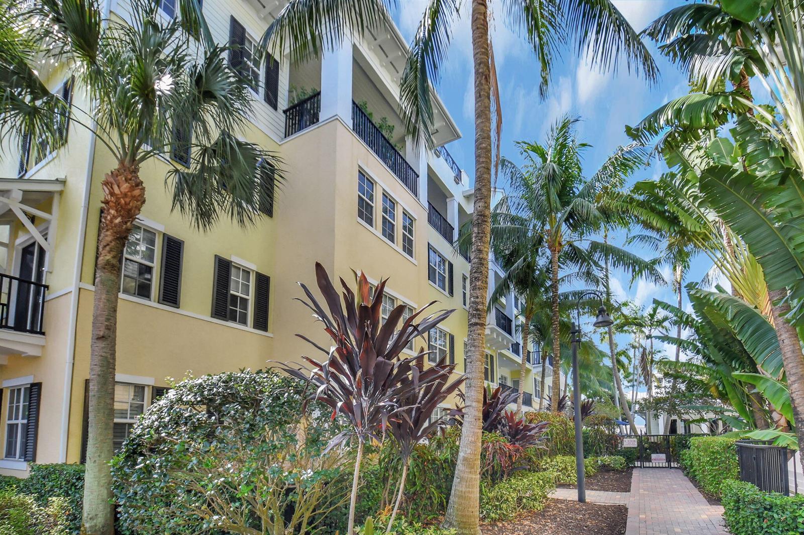 A multi-story yellow apartment building is surrounded by palm trees and lush tropical landscaping — 3120 E Latitude Circle # 307, Delray Beach FL 33483, DELRAY BEACH, FL