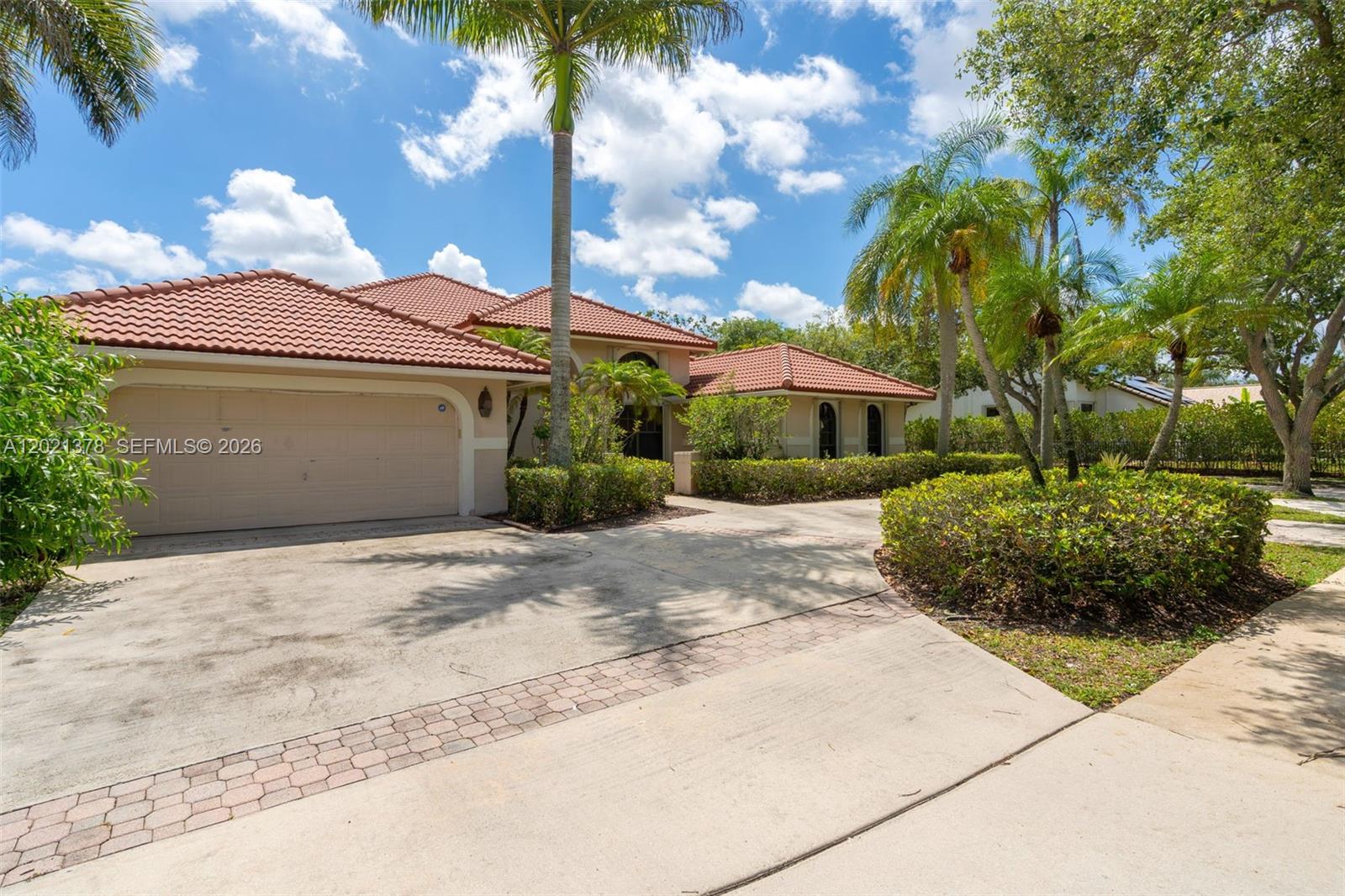A single-story house with a tile roof, two-car garage, and palm trees in the front yard — 1051 Deerpath Ct, Weston FL 33326, WESTON, FL