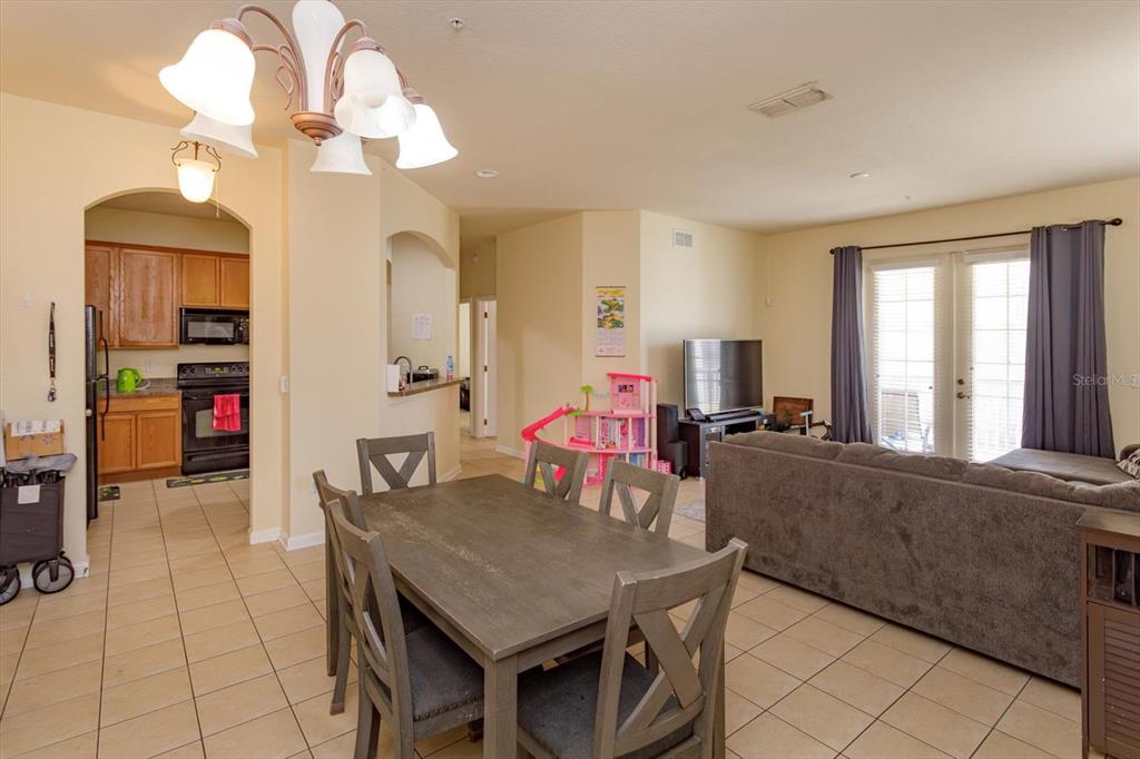 An open-concept living and dining area features tile flooring, a wooden table, and a kitchen — 3001 LAUREL RUN LANE UNIT 206, KISSIMMEE, FL