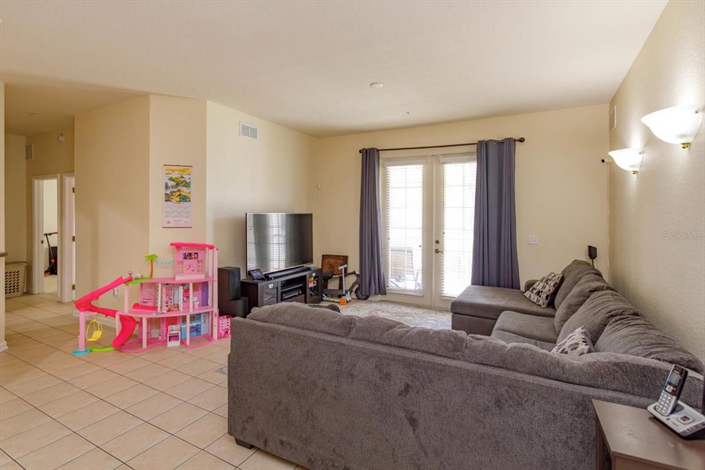 A living room features a gray sectional sofa, a television on a stand, and a dollhouse — 3001 LAUREL RUN LANE UNIT 206, KISSIMMEE, FL