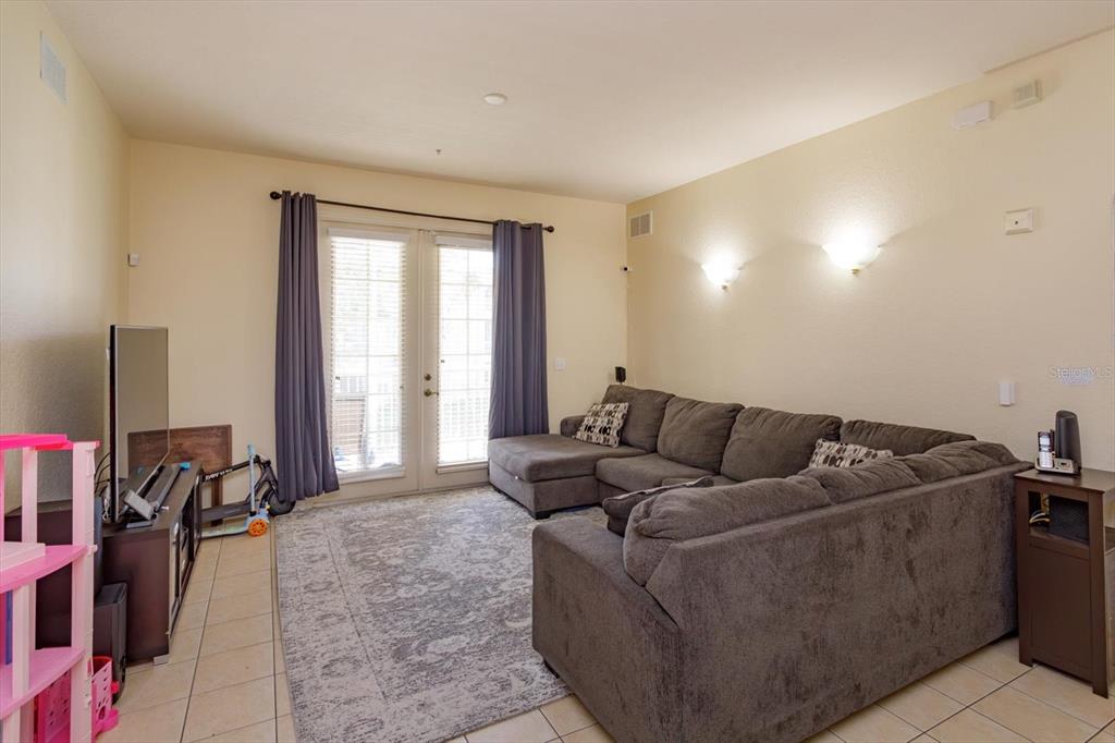 A living room features a large gray sectional sofa, a patterned area rug, and glass doors — 3001 LAUREL RUN LANE UNIT 206, KISSIMMEE, FL
