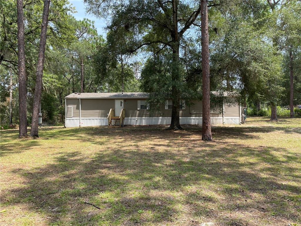 A beige metal storage shed with a red roll-up door sits in a wooded area — 8089 SW 147TH LANE, DUNNELLON, FL