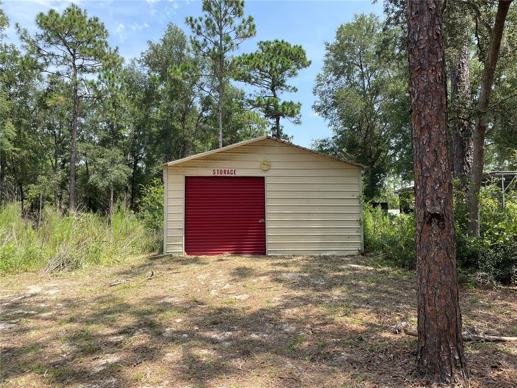 A single-wide mobile home with a red door and shutters sits on a wooded lot — 8089 SW 147TH LANE, DUNNELLON, FL