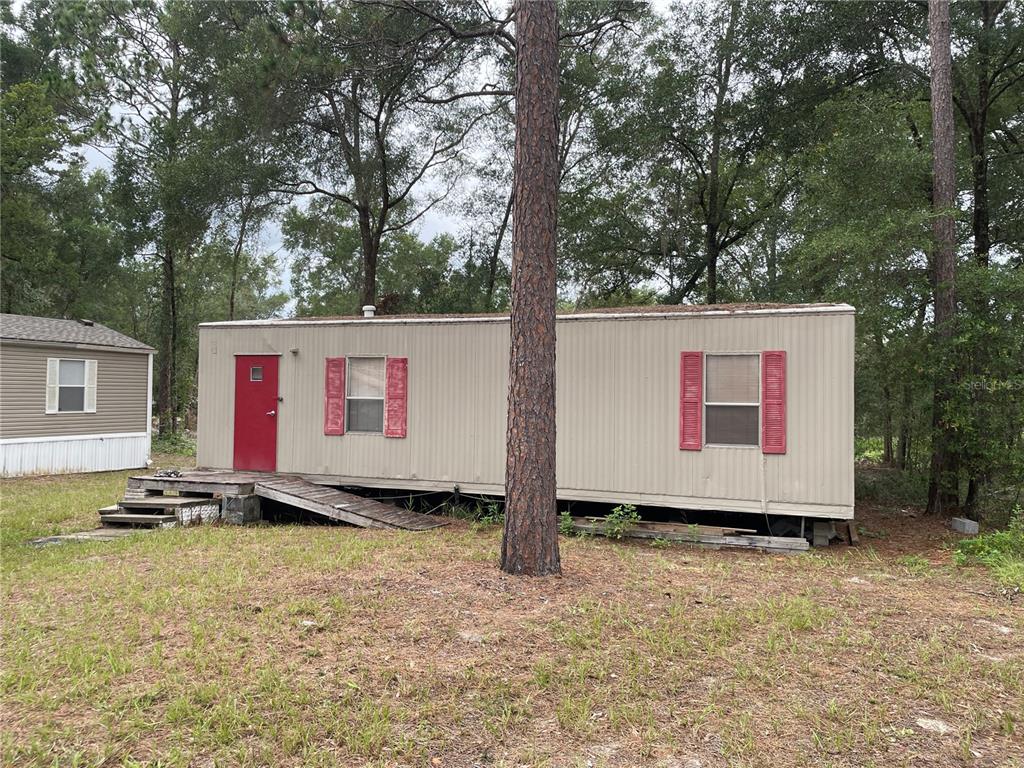 A single-story manufactured home with tan siding sits on a grassy lot among many trees — 8089 SW 147TH LANE, DUNNELLON, FL