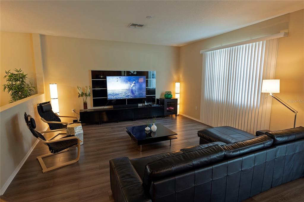 A modern living room features dark wood flooring, a black leather sofa, and a television — 1039 TOURMALINE DRIVE, KISSIMMEE, FL
